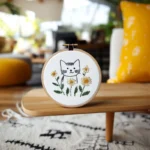 A cat and daisy embroidery piece displayed on the coffee table in the living room.
