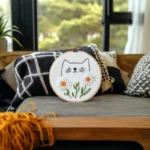 A daybed with a blanket, throw pillows, and an embroidery piece