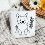 A puppy and wildflower embroidered throw pillow placed on a blanket as a decorative piece.