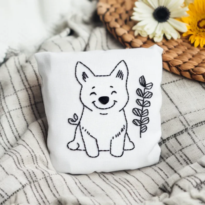 A puppy and wildflower embroidered throw pillow placed on a blanket as a decorative piece.