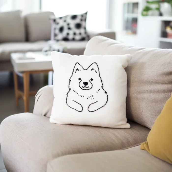 A white bear embroidered throw pillow placed on a khaki-colored sofa.