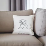 A white throw pillow on a khaki-colored sofa, featuring an embroidered dog gazing into the distance.