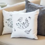 A sofa with three pillows, two of which are white and embroidered with bird and branch patterns