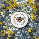 Bee and floral wreath embroidery displayed on floral fabric, accented with chrysanthemums