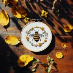 Bee and floral wreath embroidery placed on a table, decorated with fallen leaves