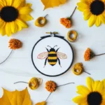 Bee embroidery artwork displayed on a table, accented by sunflowers and fresh flowers nearby