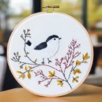 Close-up of a black and white bird embroidery perched on yellow and red autumn branches