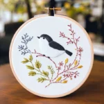 Close-up of an embroidery artwork featuring a bird perched on a tree branch