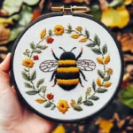 Hand holding a bee and floral wreath embroidery artwork