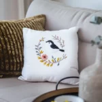 Minimalist gray sofa with a golden pillow and a white fabric pillow embroidered with a bird and branch design