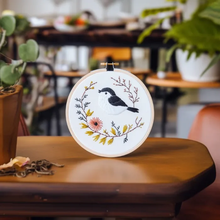 Room filled with green plants and a table displaying a bird and floral tree embroidery piece