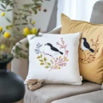 Soft and colorful bird-themed embroidered pillows placed on a gray sofa