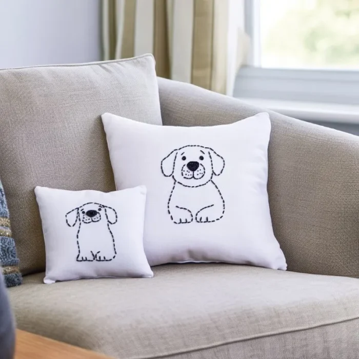 White throw pillows with embroidered line art of a Labrador dog on a sofa — one large, one small