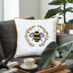 Leafy foreground, with a bee wreath embroidered pillow on a sofa and a potted plant in the background