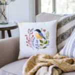 A bright living room with a floor-to-ceiling window, featuring a sofa with bird and floral embroidered pillows and a cozy throw