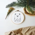 Brown bear and wild grass embroidery piece on white floor with decorative plants and fabric