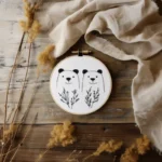 Smiling bear embroidery art with decorative plants arranged on a wooden surface