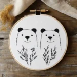 Two smiling bear hand embroidery pieces displayed on a tabletop