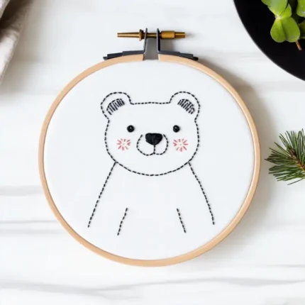 Adorable blushing bear embroidery in a hoop, stitched on clean white fabric in soft lighting