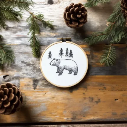 Bear embroidery piece on a table decorated with pine branches and pinecones