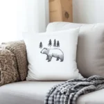 Bright and cozy living room with a light gray sofa, a white pillow embroidered with a bear and pine trees, and a gray-and-white striped throw blanket