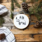 Hand-stitched bear embroidery surrounded by pine branches and pinecones, evoking the power of nature