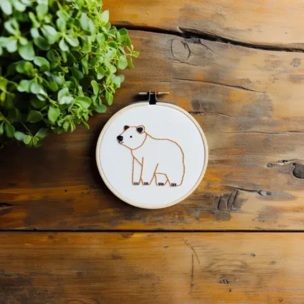 Handmade bear embroidery artwork centered on the table, decorated with a small cluster of autumn leaves nearby