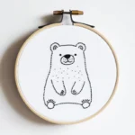 Handmade bear embroidery in a hoop on white fabric, featuring a gentle bear quietly gazing forward