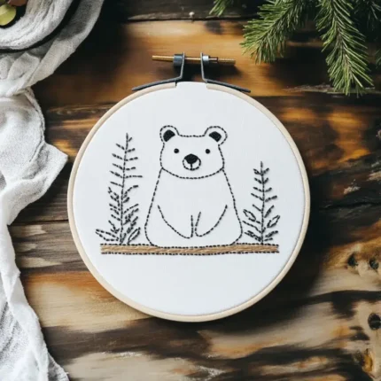 Handmade bear embroidery showing a calm little bear sitting between two pine trees, evoking a sense of safety