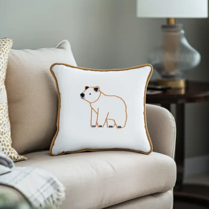 Khaki-colored sofa with a gold-trimmed embroidery pillow featuring a bear outlined in golden thread