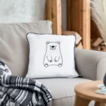 Modern living room with a gray sofa, a white fabric pillow featuring black line bear embroidery, and a gray-white-black patterned throw blanket