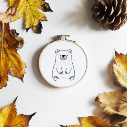Minimalist bear line art embroidery placed in the center, accented with dried maple leaves