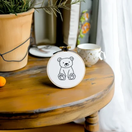 Small round table with bear embroidery artwork, a coffee cup, and a potted plant