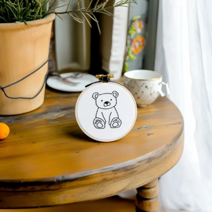Small round table with bear embroidery artwork, a coffee cup, and a potted plant