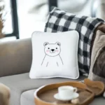Sunlight streaming through glass onto a gray sofa with a small white bear embroidery pillow