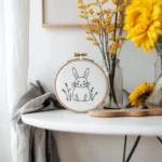 Embroidered rabbit design fixed in a hoop on the table, decorated with chrysanthemums