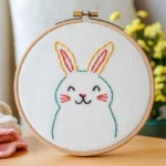 Handmade embroidery of a cute rabbit with closed eyes smiling, placed on a wooden table