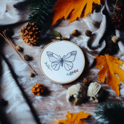 minimalist butterfly embroidery on table with pinecones and pine leaves