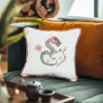 Green sofa with two pillows, one in orange and the other a white embroidered pillow featuring a dragon
