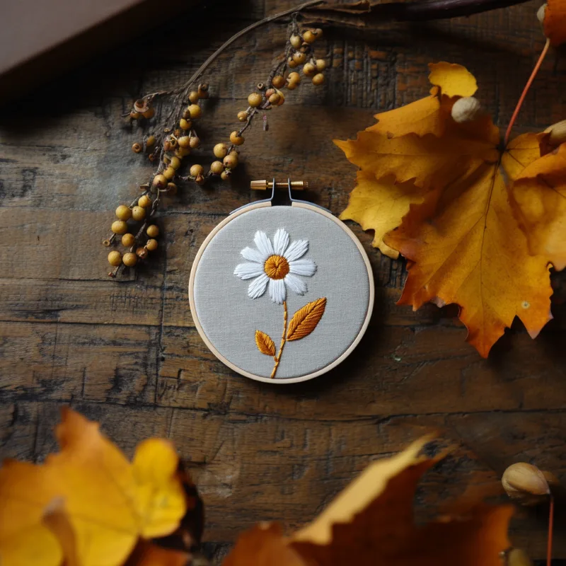 daisy embroidery piece on a table with autumn leaves and branches as decoration Modern Daisy Embroidery DIY Pattern Instant Download - Image 2