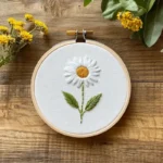 daisy hand embroidery artwork displayed on a wooden table