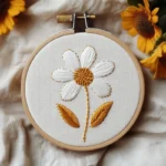 finished handmade embroidery featuring a daisy with golden leaves