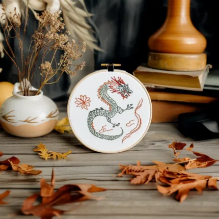 Green dragon hand embroidery displayed on a wooden table with flowers and fallen leaves as decoration