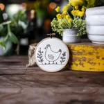 minimalist embroidery on a wooden table with two potted plants in the background