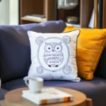 two pillows on a dark blue sofa, one orange and one white embroidered with an owl