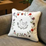 white cushion on a sofa embroidered with flowers encircling a chicken