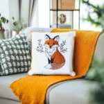white pillow embroidered with a fox, placed on an orange blanket