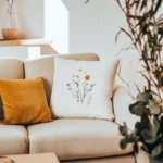 a beige sofa with a white embroidered pillow and a warm ginger-colored pillow