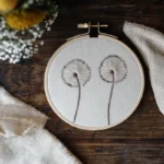 a hand-embroidered dandelion artwork displayed on a table