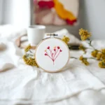 a hand embroidery piece on the table, with a cup beside it and a framed artwork in the background